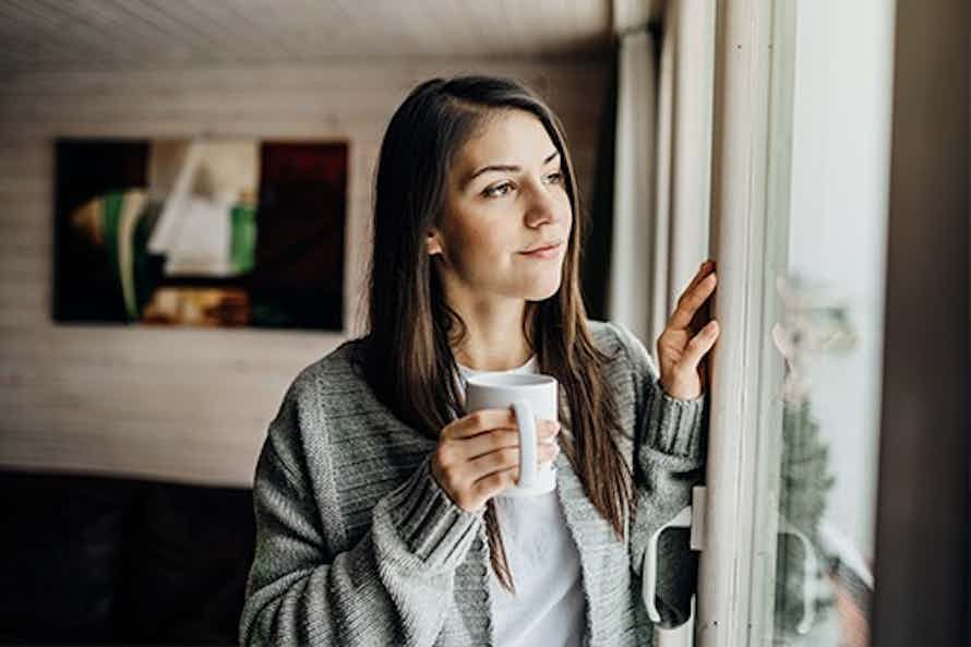 Woman looking outside with a cup of coffee